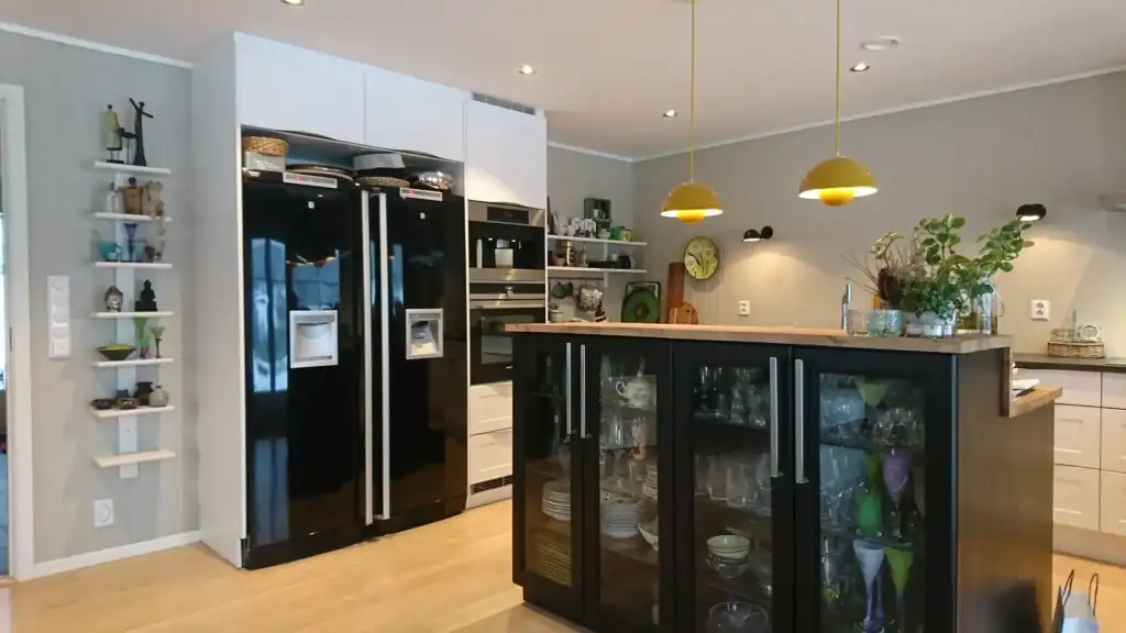 Lys innbydende moderne kjøkkenstil med svarte og hvite skap, treverk bordflate og gulv, dekorative grønne planter og strømbelysning.