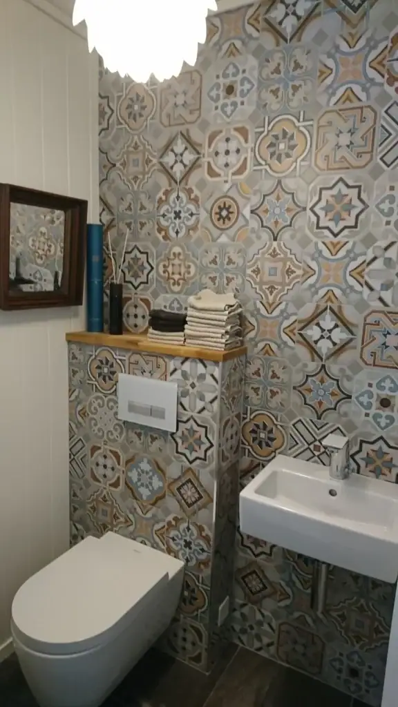 Fargerik bademaling med mønstrede fliser, liten vask og toalett på bad i moderne boligmiljø.