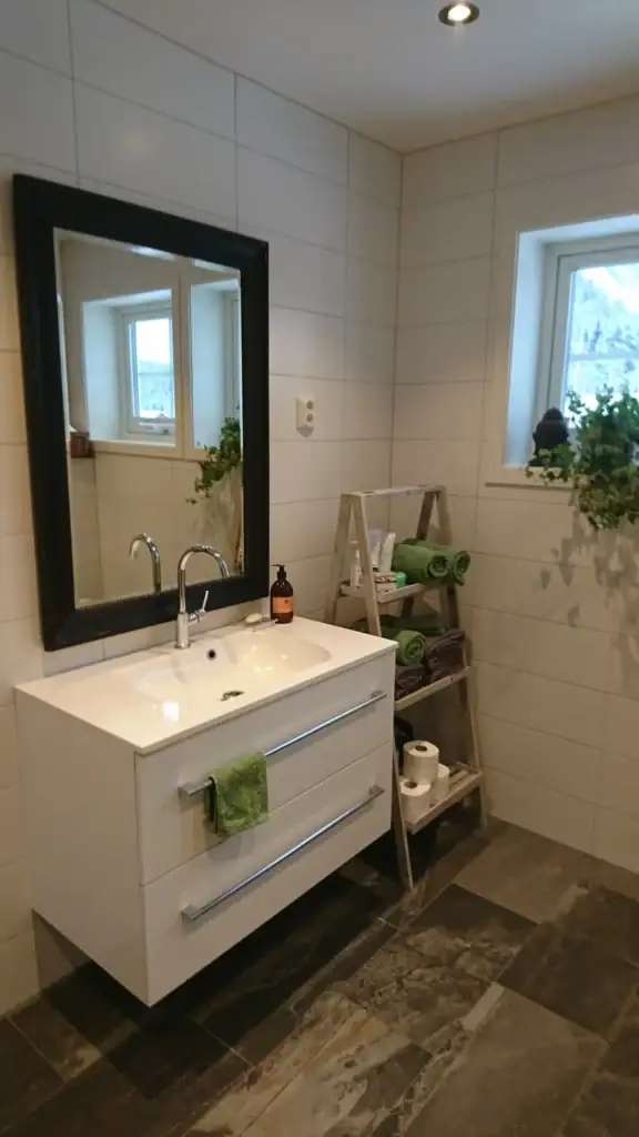 Moderne baderom med vask, speil og grønne håndklær.