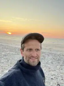 Bilde av en mann på stranden under solnedgang, viser en fredelig og naturlig atmosfære for utendørsaktiviteter og avslapning.