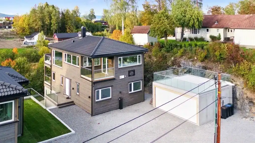 Moderne bolig med energismart design og store vindusflater, omgitt av naturskjønnhet og grøntarealer i en rolig nabolagsatmosfære.