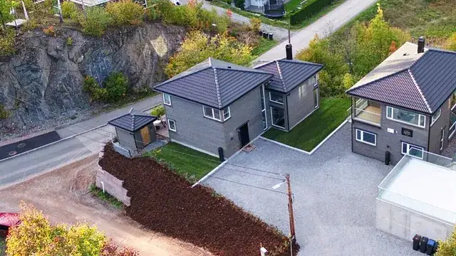 Moderne bolighus med grasplen og oppkjørsel i naturskjønt område, fotografert fra luften.