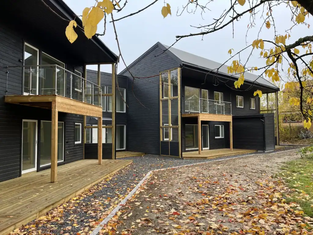 Modern black wooden residential building with glass balconies and wooden decks during autumn.